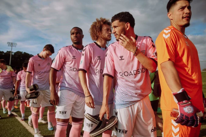 A line of soccer players in pink and white uniforms walking on a field under a bright sky, showcasing team unity and sportsmanship.