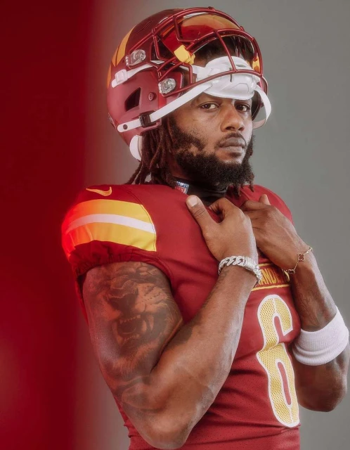 Close-up portrait of a male American football player in burgundy uniform and helmet looking intensely at the camera. 