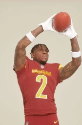Football player wearing burgundy jersey number 2 and white gloves holding a football over his head