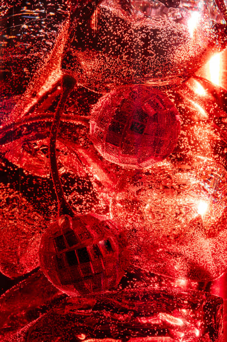 Close-up of two disco balls in a bright red liquid with bubbles, creating an abstract and festive visual effect.