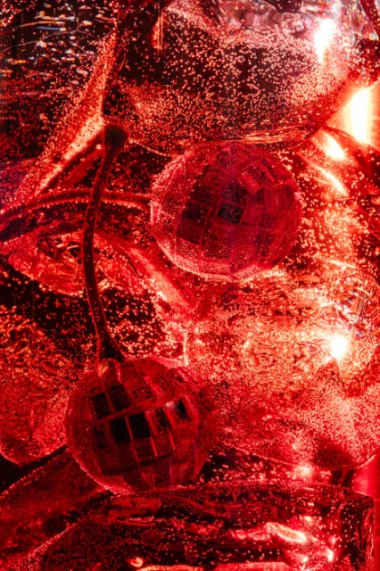 Close-up of two disco balls in a bright red liquid with bubbles, creating an abstract and festive visual effect.