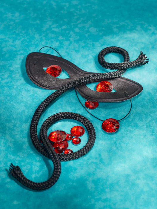 Still life of a masquerade mask, black rope, and red gemstones on an textured teal background with soft lighting, creating a theatrical mood.