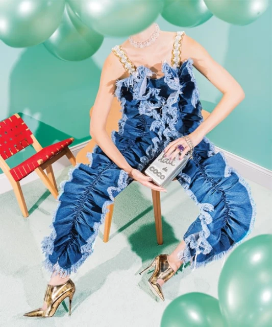 Woman in a denim jumpsuit sits with Lait de Coco box, metallic heels, surrounded by green balloons against a turquoise wall.