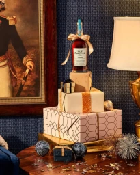 A liquor bottle on a stack of wrapped gift boxes next to a framed portrait and a lamp in Los Angeles.