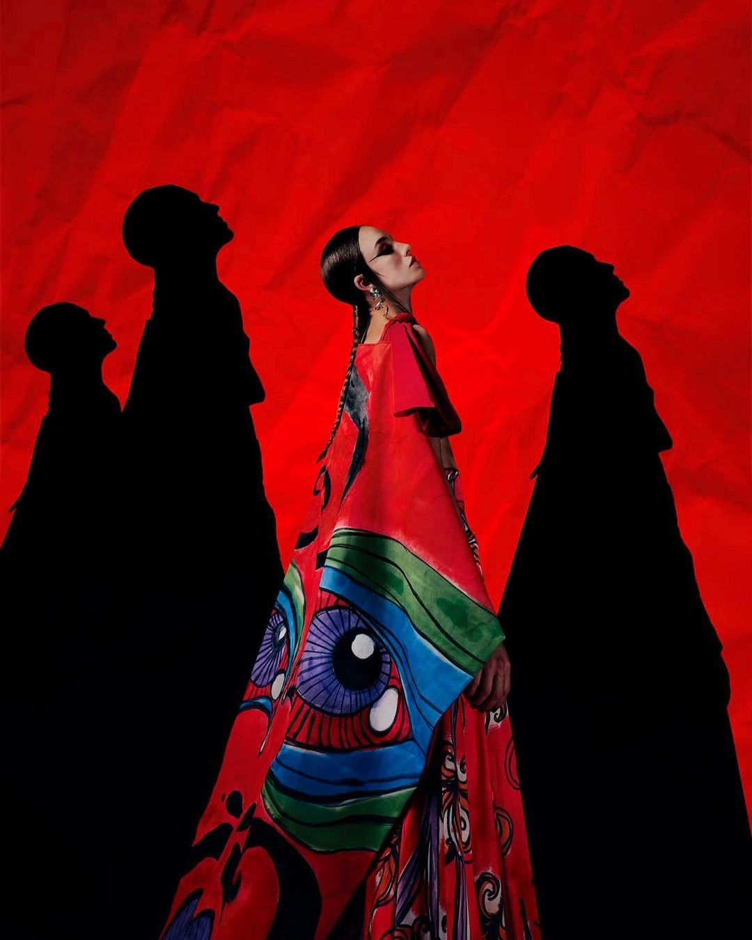 Fashion photo of a woman in a red and patterned kimono looking up, with silhouetted figures against a textured red backdrop.