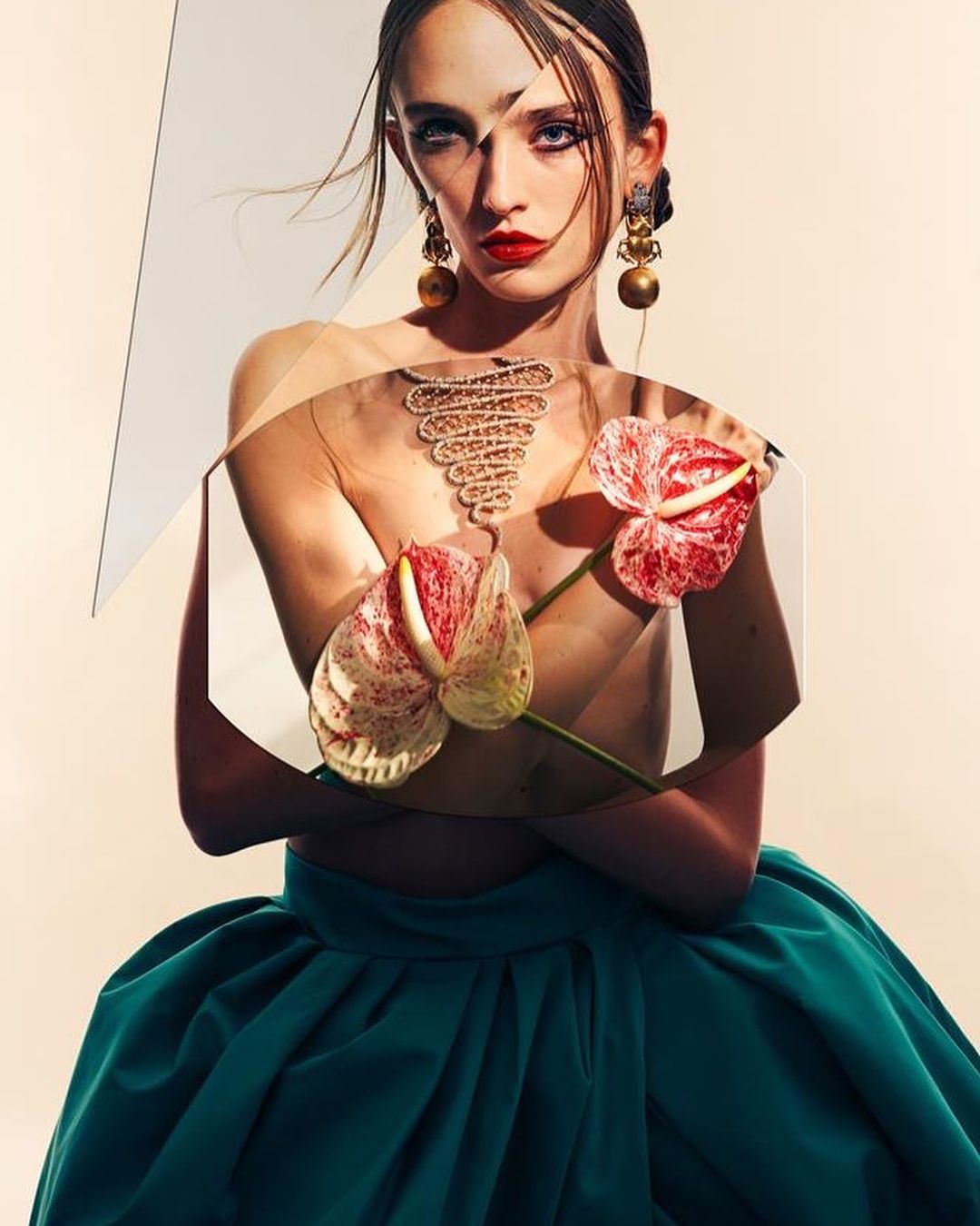 Fashionable woman in a green skirt and statement earrings poses with Anthurium flowers in a studio, geometric shapes adding to the look.