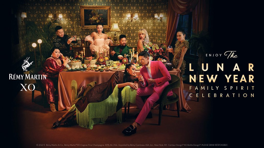 Elegant indoor celebration featuring a diverse group of people gathered around a table with drinks and food, styled with gold accents.