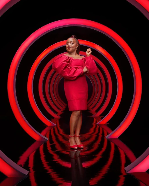 Smiling woman in a red dress posing confidently against a backdrop of concentric red circles, creating a vibrant and stylish portrait.