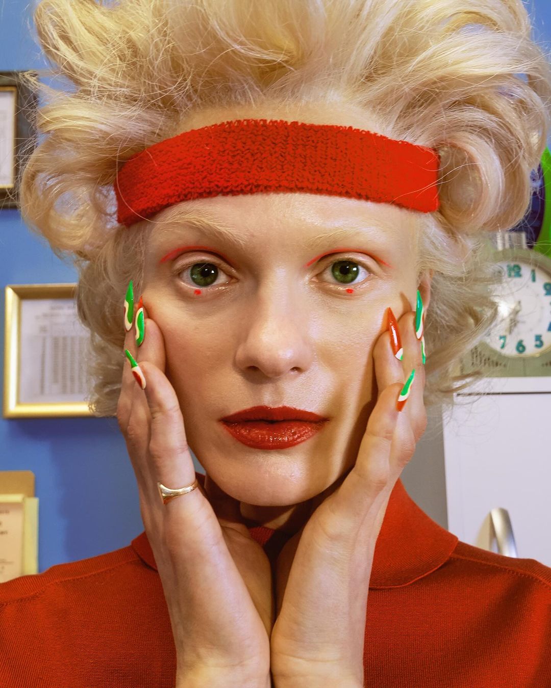Close-up portrait of a fair-skinned adult female with retro red and green nail art, red lipstick, and a matching red headband.