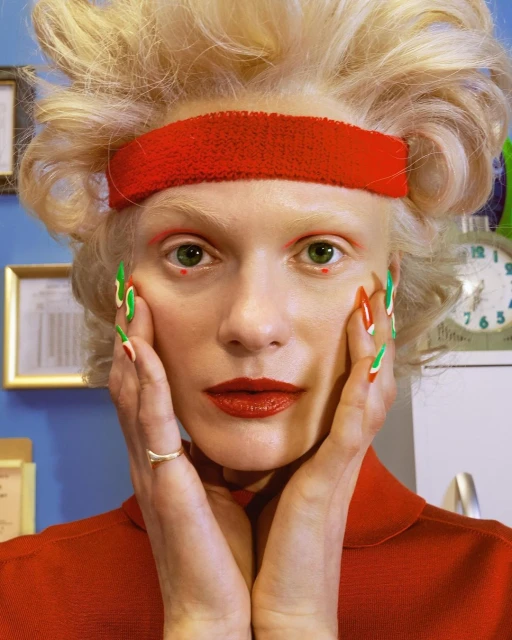 Close-up portrait of a fair-skinned adult female with retro red and green nail art, red lipstick, and a matching red headband.