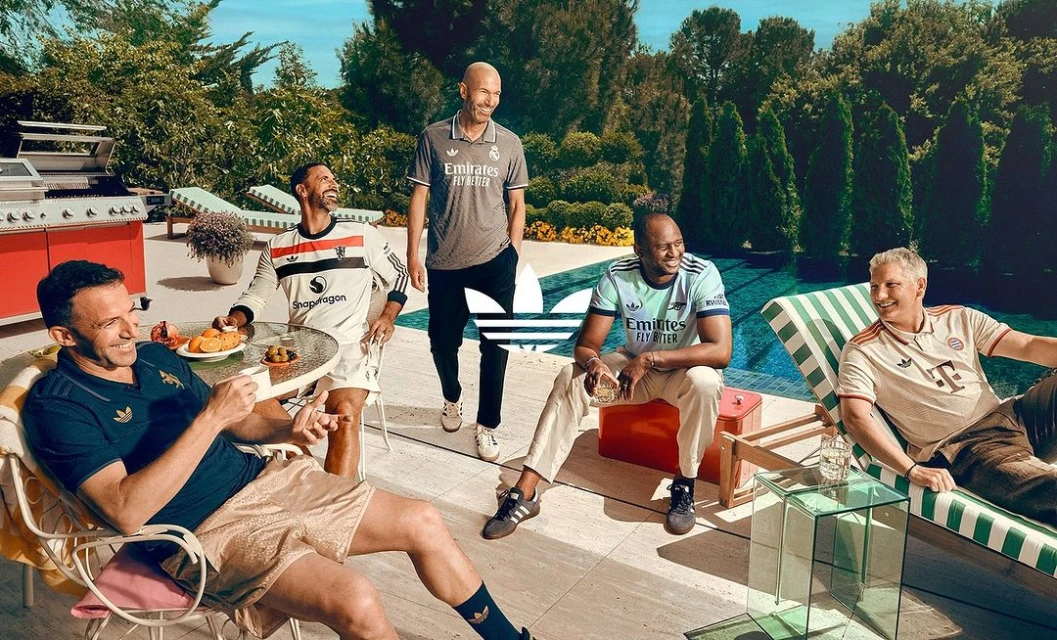 Group of soccer legends relaxing poolside in Adidas apparel, featuring Zidane, with lush greenery, bright lighting, and brand visibility.