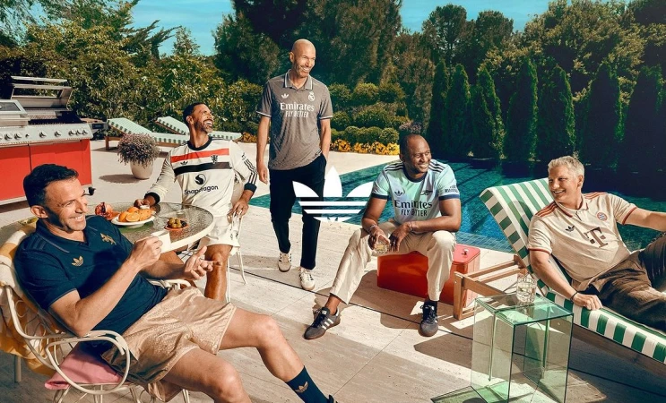 Group of soccer legends relaxing poolside in Adidas apparel, featuring Zidane, with lush greenery, bright lighting, and brand visibility.