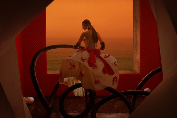 Woman in a large white dress with red accents stands inside a modern orange and white structure with the ocean in the background.