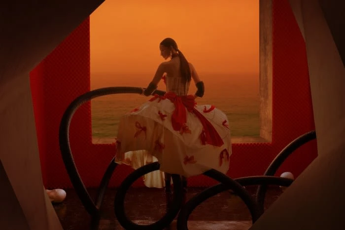 Woman in a large white dress with red accents stands inside a modern orange and white structure with the ocean in the background.