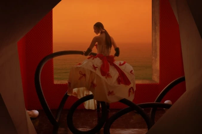 Woman in a large white dress with red accents stands inside a modern orange and white structure with the ocean in the background.