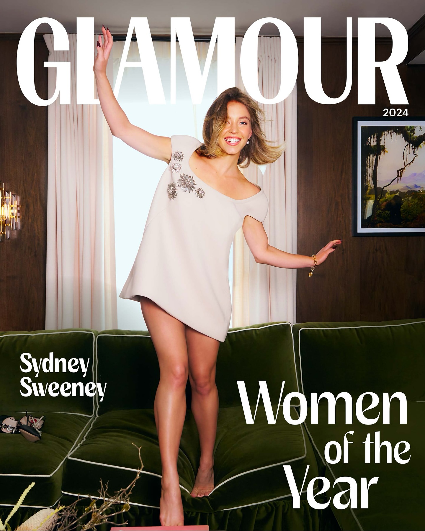 Glamour magazine cover featuring Sydney Sweeney jumping on a green velvet couch in a white mini dress with floral accents, 2024.