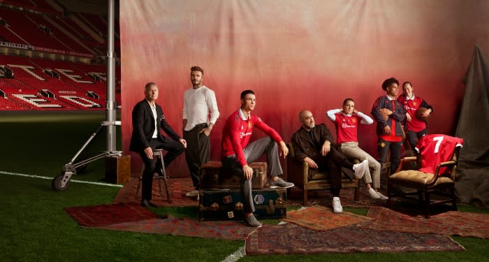 Group portrait of soccer players and coaches, including Cristiano Ronaldo and David Beckham, in a stadium with a reddish backdrop.