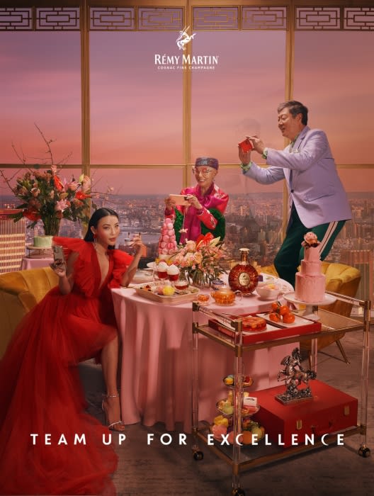 Three people at a table in a high-rise setting with a view, sharing pastries, taking photos with cell phones, and posing for Rémy Martin ad.