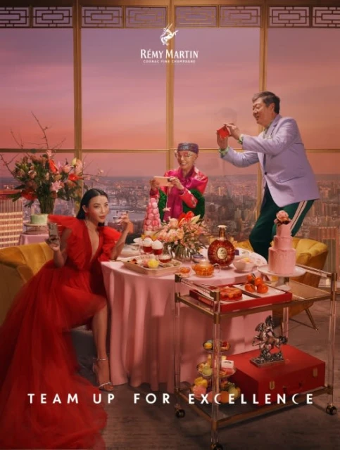 Three people at a table in a high-rise setting with a view, sharing pastries, taking photos with cell phones, and posing for Rémy Martin ad.