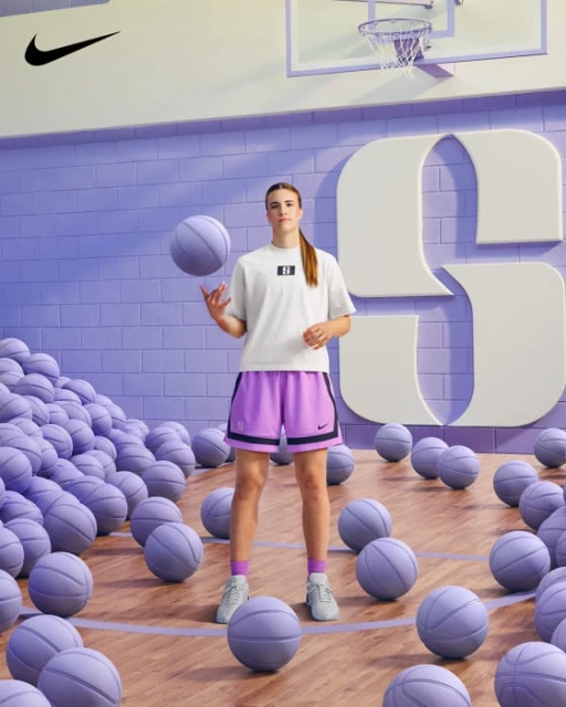 Young woman in athletic wear spins a basketball in a purple and cream basketball court filled with basketballs and branded backdrop.