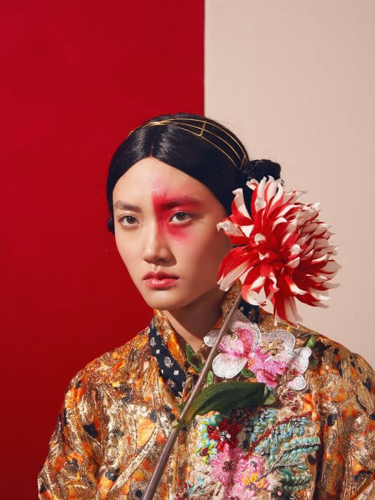 Close-up studio shot of an Asian female model with dramatic makeup, a gold headpiece, and an embroidered kimono holding a dahlia flower.