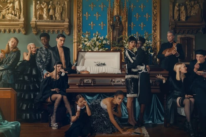 Editorial fashion shoot in a vintage interior features diverse models gathered around an open casket, evoking a solemn and stylish atmosphere.