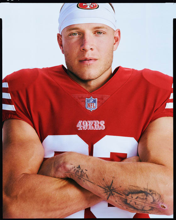 Portrait of a muscular adult male football player in a red uniform and white headband with arms crossed against a light background.
