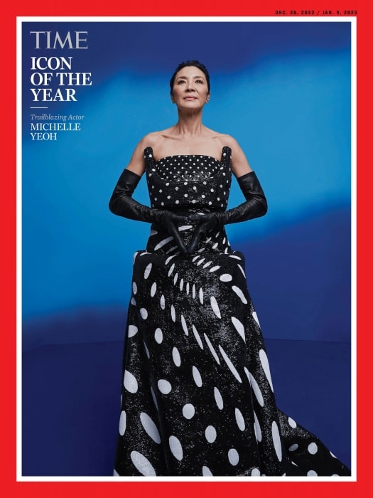 Michelle Yeoh, TIME's Icon of the Year, poses in a black and white polka dot gown and long gloves against a blue gradient background.