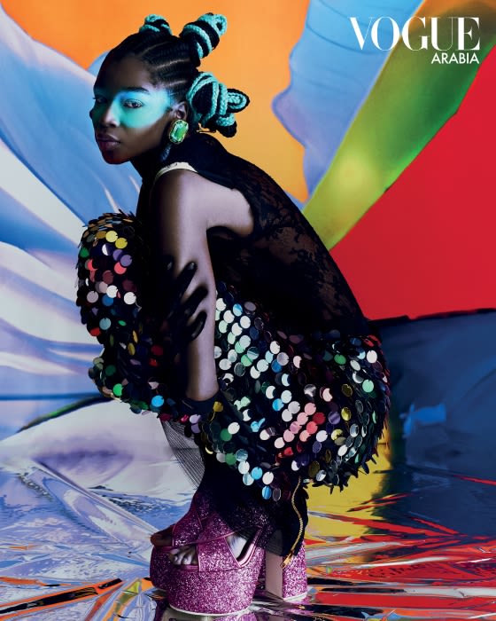 Vogue Arabia cover featuring a black woman with unique hair, makeup, and a shiny dress, posing in front of an abstract colorful background.