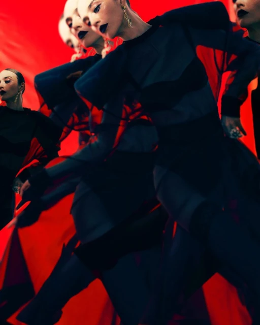 Dynamic fashion image: multiple women in dark tops with red accents against a vivid red backdrop, showcasing movement and style.