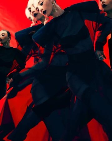 Dynamic fashion image: multiple women in dark tops with red accents against a vivid red backdrop, showcasing movement and style.