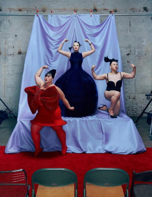 Three plus-size women strike poses in a studio setting. One wears a red dress with an oversized bow, another a blue gown, and another a black bodysuit.