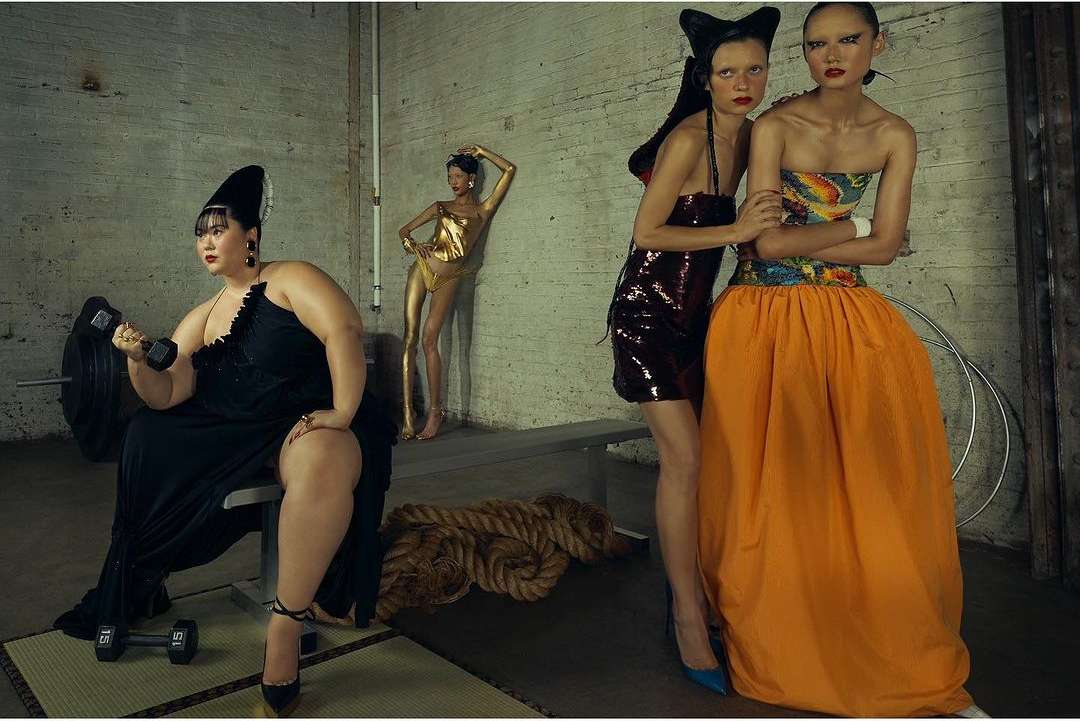 Four women pose in an industrial space with a rope, barbell and dumbbells, showcasing high fashion with athletic equipment for editorial purposes.