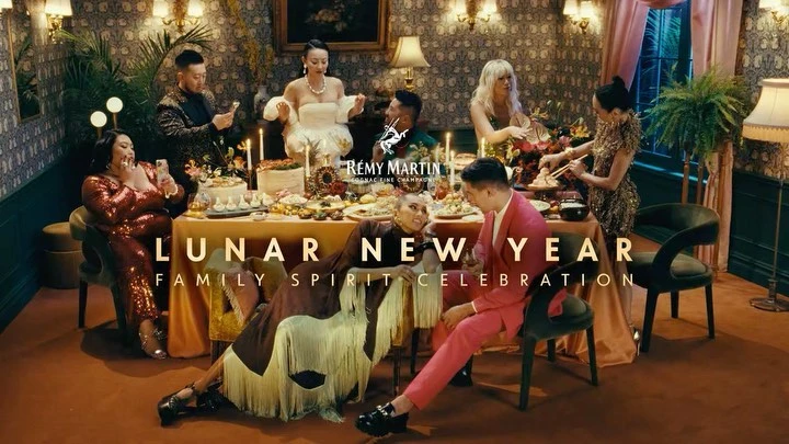 A group of diverse people sit around a table laden with food and beverages celebrating the Lunar New Year in a warm, inviting setting.