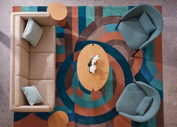 Overhead shot of contemporary living room arrangement with beige sofa, two chairs, round tables, and patterned rug in brown, teal, and blue.