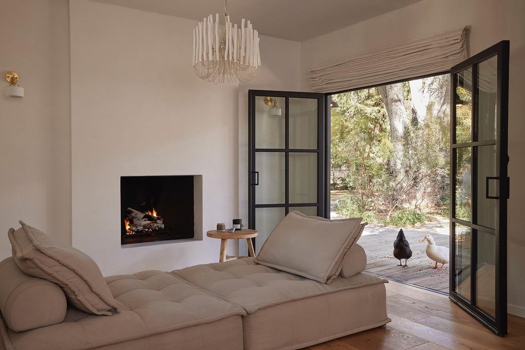 Living room interior with a beige sectional sofa, fireplace, and open doors to an outdoor area with two ducks visible.