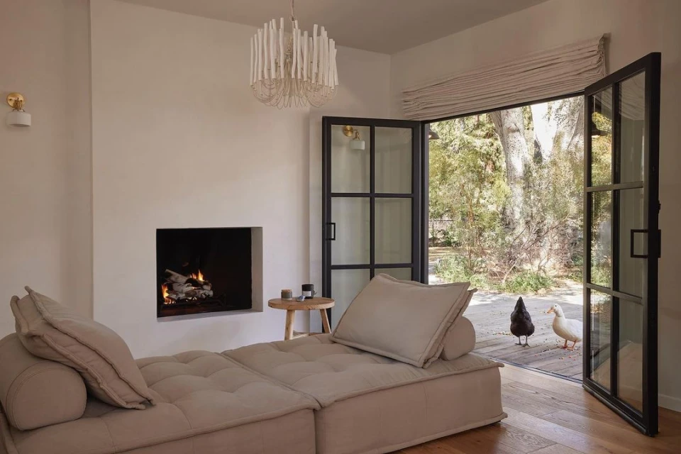 Living room interior with a beige sectional sofa, fireplace, and open doors to an outdoor area with two ducks visible.