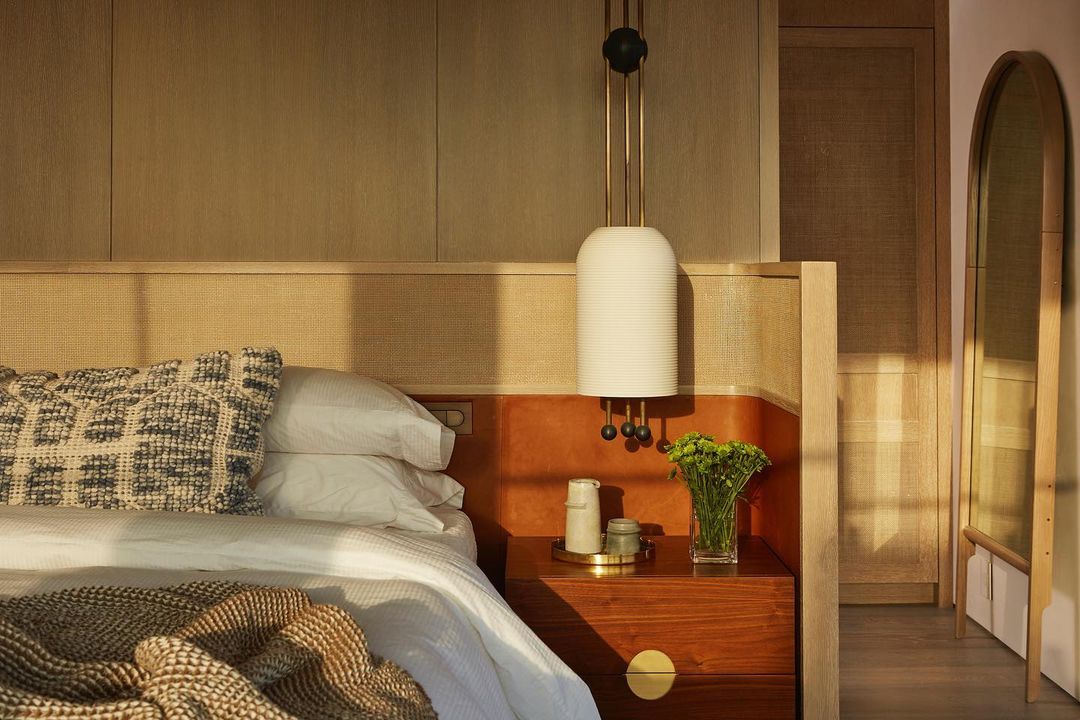 Bedroom interior showcasing a made bed with decorative pillow and throw, a bedside table with a lamp, and an arched mirror.
