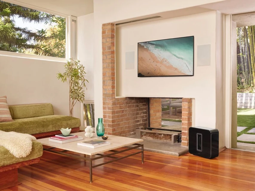 Living room interior with a modern sofa, wooden floor, brick fireplace, and a flat-screen television displaying a beach scene.