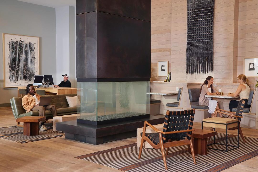 Interior view showcases a lounge area with people relaxing on sofas and chairs, complemented by a unique fireplace and modern design.