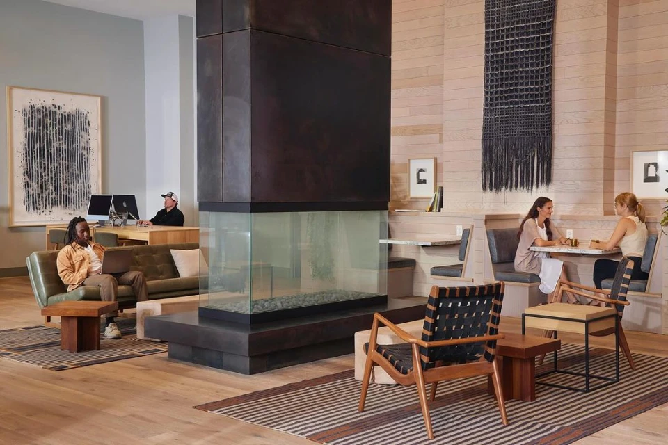 Interior view showcases a lounge area with people relaxing on sofas and chairs, complemented by a unique fireplace and modern design.