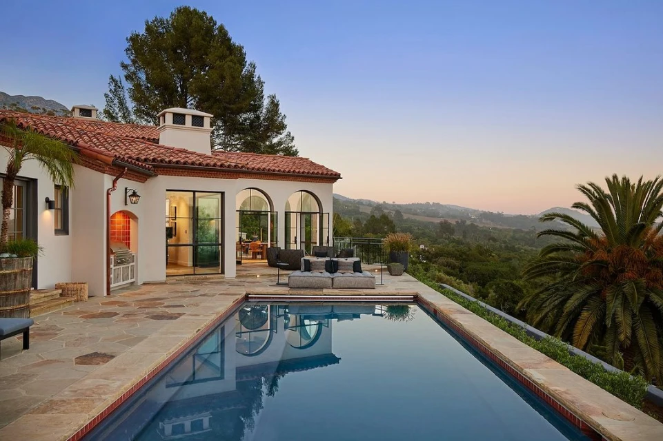 Exterior view of a luxury home with a swimming pool, featuring architectural details, landscaping, and a scenic view of the mountains.
