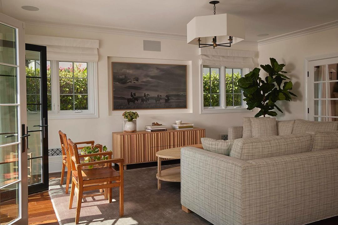 Living room interior showcasing a neutral sectional sofa, wooden chairs, and a cabinet with art above in a well-lit, comfortable space.