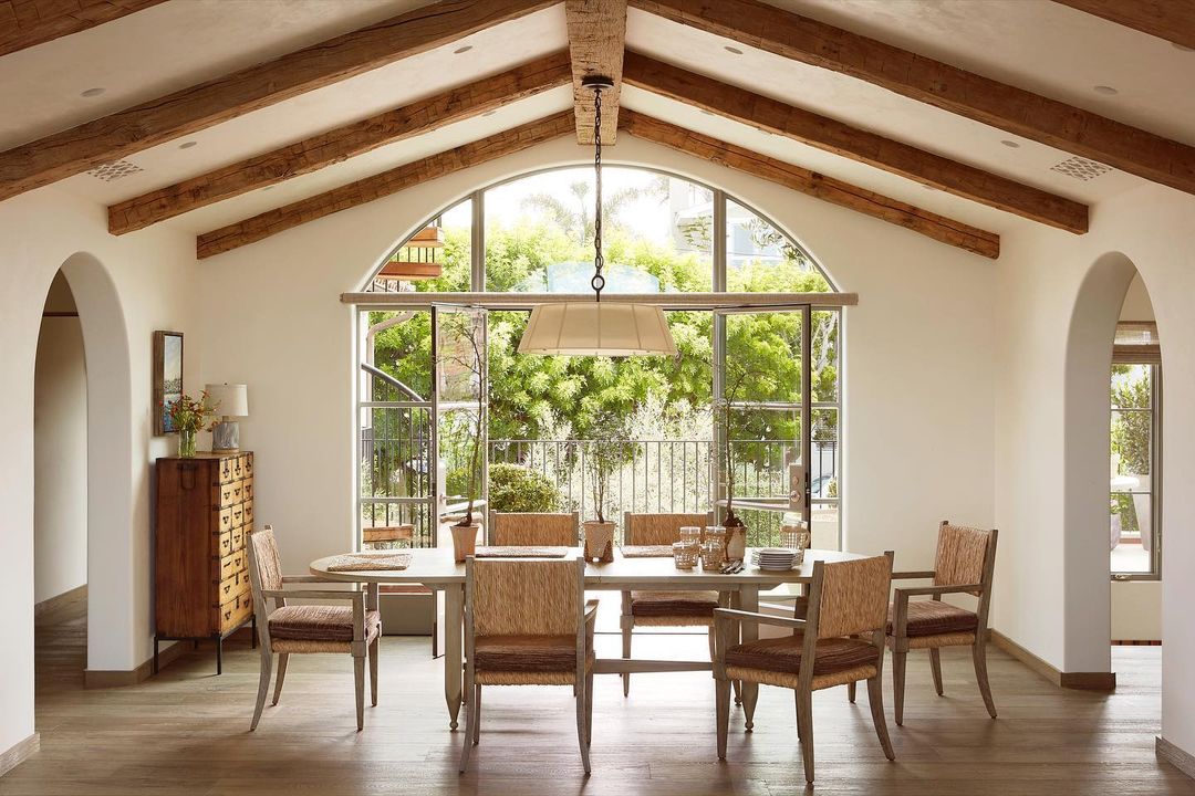 Dining room featuring a long wooden table with seating for six, complemented by woven chairs and a view to a garden.