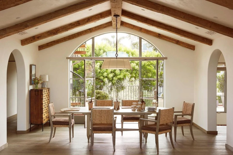 Dining room featuring a long wooden table with seating for six, complemented by woven chairs and a view to a garden.