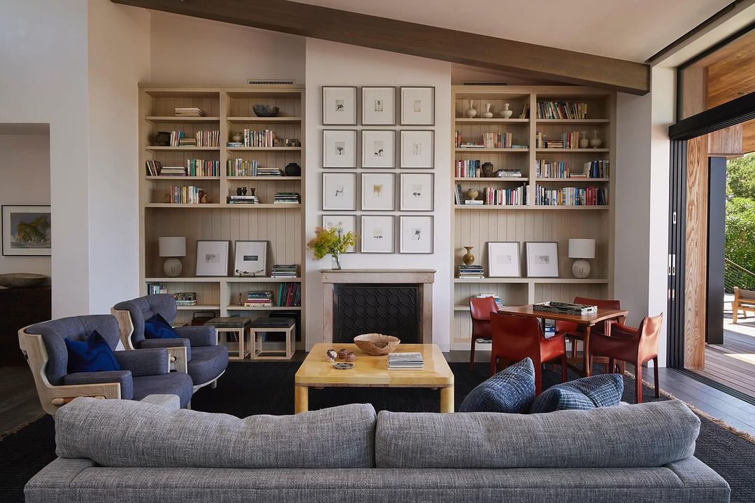 Living room interior with gray sofa, bookshelves, fireplace, and natural light, creating a cozy and inviting atmosphere.