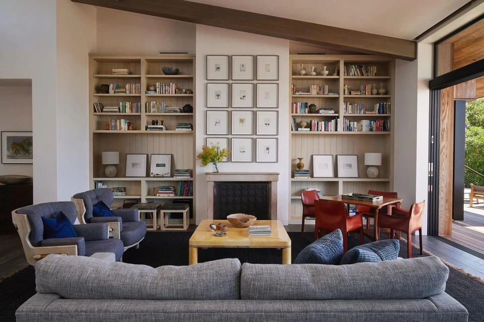 Living room interior with gray sofa, bookshelves, fireplace, and natural light, creating a cozy and inviting atmosphere.