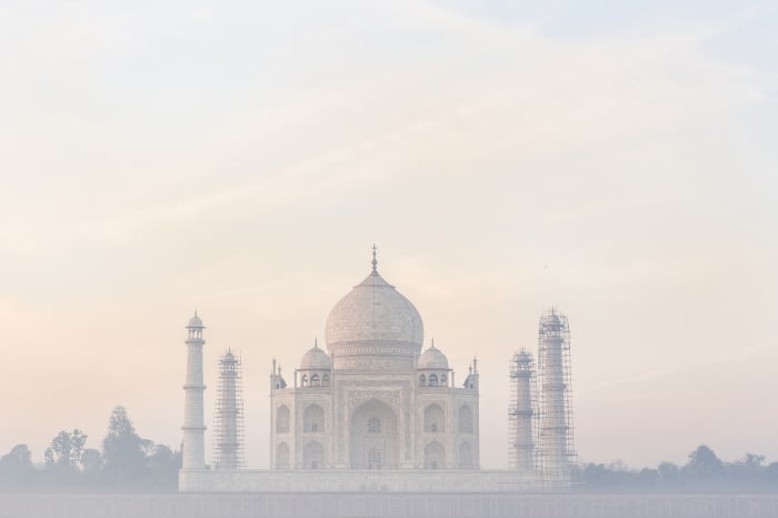 The Taj Mahal in Agra, India, is seen at eye-level in a wide shot. Its white marble architecture contrasts with the soft sky in this image.