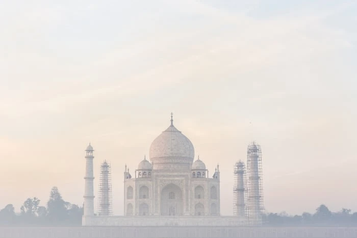 The Taj Mahal in Agra, India, is seen at eye-level in a wide shot. Its white marble architecture contrasts with the soft sky in this image.