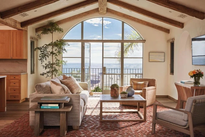 Cozy living room with natural light, featuring a grey couch, wooden coffee table, and a view of the ocean through large windows.